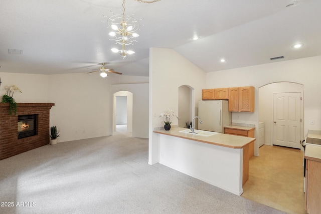 kitchen featuring arched walkways, freestanding refrigerator, a sink, light countertops, and vaulted ceiling