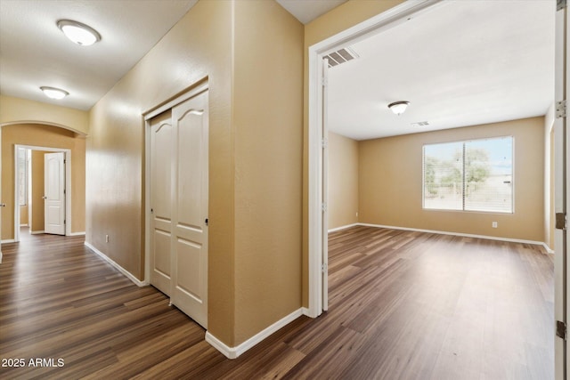hallway with dark wood-type flooring, arched walkways, and baseboards