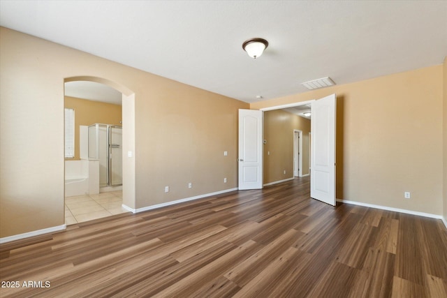 unfurnished bedroom featuring arched walkways, wood finished floors, and baseboards