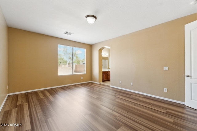empty room with arched walkways, wood finished floors, and baseboards