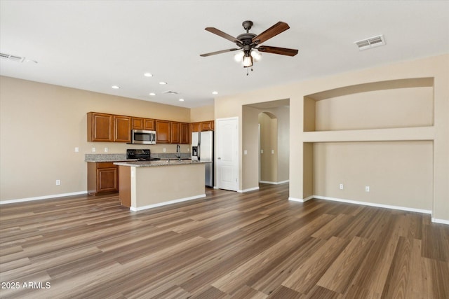 kitchen with stainless steel appliances, open floor plan, brown cabinets, arched walkways, and a ceiling fan