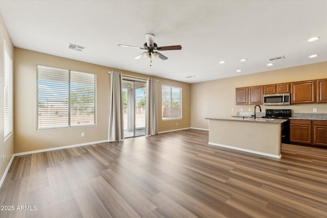 kitchen with stainless steel microwave, open floor plan, black electric range, a ceiling fan, and brown cabinetry