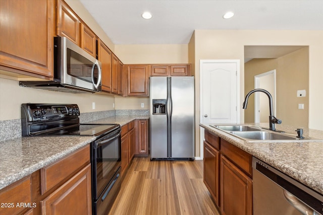 kitchen featuring stainless steel appliances, a sink, brown cabinets, light wood-style flooring, and recessed lighting
