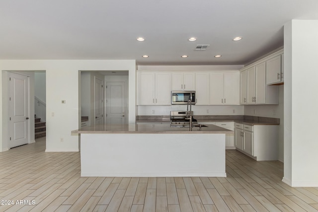 kitchen featuring a center island with sink, white cabinetry, light hardwood / wood-style flooring, and stainless steel appliances