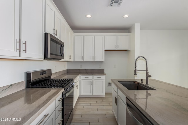 kitchen with light stone counters, stainless steel appliances, sink, and white cabinets