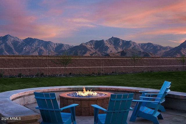 patio terrace at dusk featuring an outdoor fire pit, a mountain view, and a yard