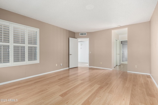 spare room with a textured ceiling, baseboards, visible vents, and light wood-type flooring