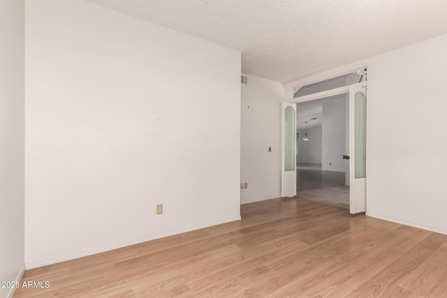 spare room featuring baseboards, light wood-style floors, arched walkways, and a textured ceiling