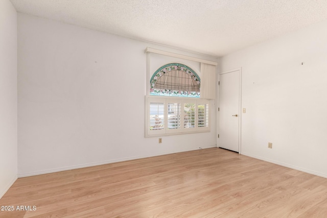 empty room featuring light wood-style flooring, baseboards, and a textured ceiling