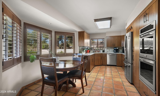 kitchen with decorative backsplash, a skylight, light tile patterned floors, and stainless steel appliances