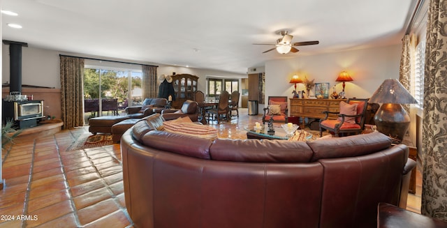 living room with a wood stove, ceiling fan, and light tile patterned floors