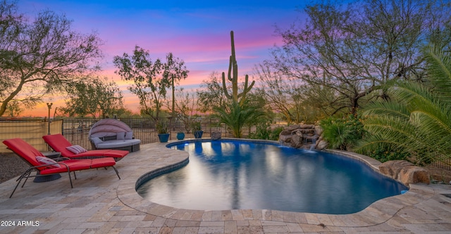 pool at dusk with a patio area and pool water feature