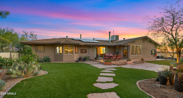 back house at dusk with solar panels, a lawn, a patio, and central air condition unit