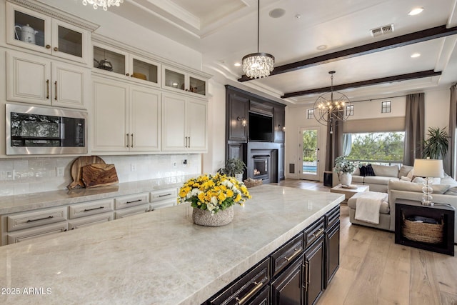 kitchen with an inviting chandelier, visible vents, light wood-style floors, stainless steel microwave, and a lit fireplace