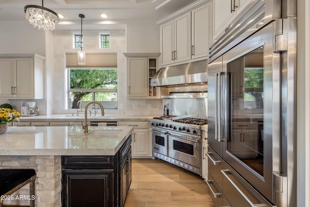 kitchen featuring light stone countertops, under cabinet range hood, light wood finished floors, decorative light fixtures, and premium appliances