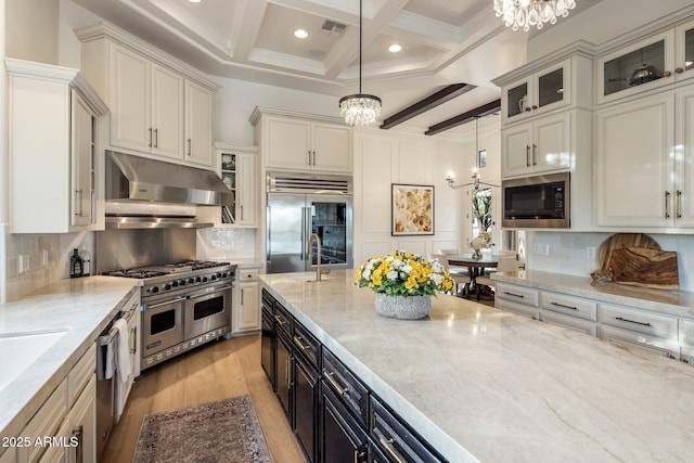 kitchen with built in appliances, under cabinet range hood, a notable chandelier, and beam ceiling