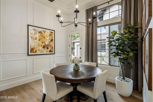 dining space featuring an inviting chandelier, ornamental molding, a decorative wall, and light wood finished floors