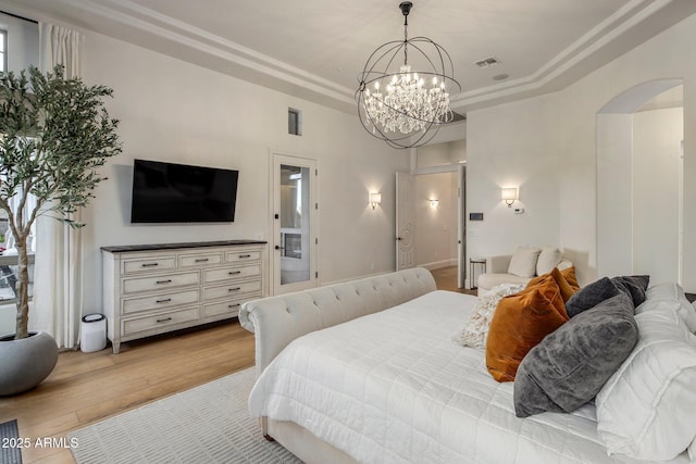 bedroom with a notable chandelier, a raised ceiling, light wood-style floors, arched walkways, and visible vents