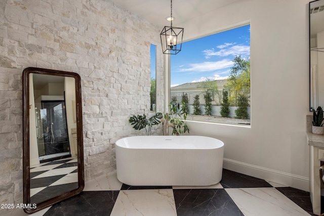 full bath with baseboards, marble finish floor, a freestanding tub, and a notable chandelier