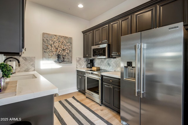 kitchen with decorative backsplash, a sink, light countertops, light wood finished floors, and stainless steel appliances