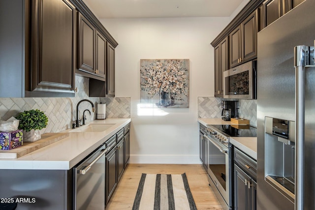 kitchen with dark brown cabinets, a sink, light countertops, stainless steel appliances, and light wood-style flooring