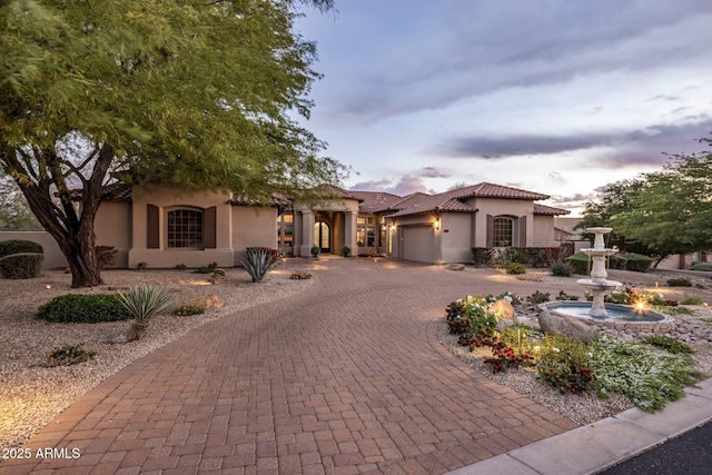 mediterranean / spanish house with a tiled roof, an attached garage, curved driveway, and stucco siding