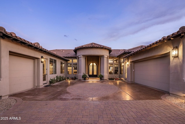 mediterranean / spanish home with an attached garage, a tile roof, stucco siding, decorative driveway, and french doors