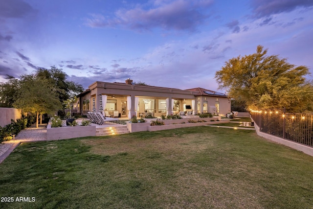 back of house at dusk featuring a yard, fence, roof mounted solar panels, and a patio area
