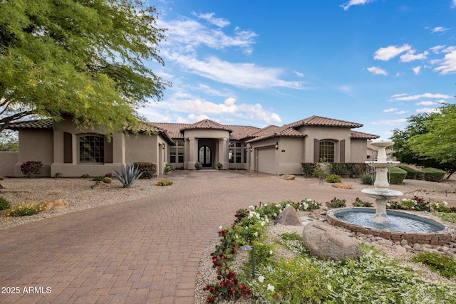 mediterranean / spanish home featuring a garage, stucco siding, decorative driveway, and a tiled roof