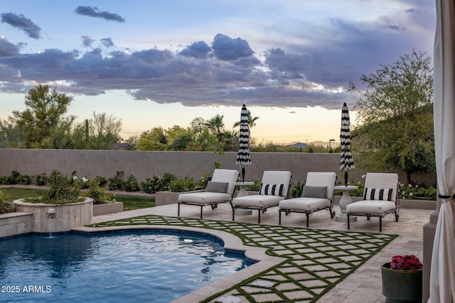 pool at dusk featuring fence, a fenced in pool, and a patio area