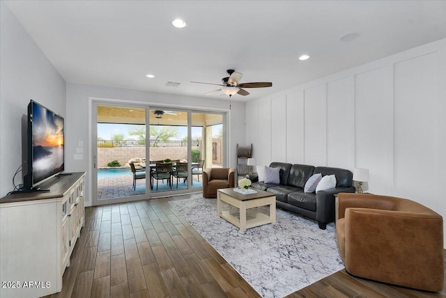 living room with a decorative wall, a ceiling fan, dark wood-type flooring, and visible vents