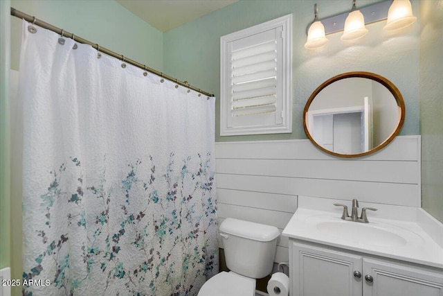 bathroom featuring toilet, curtained shower, wooden walls, wainscoting, and vanity