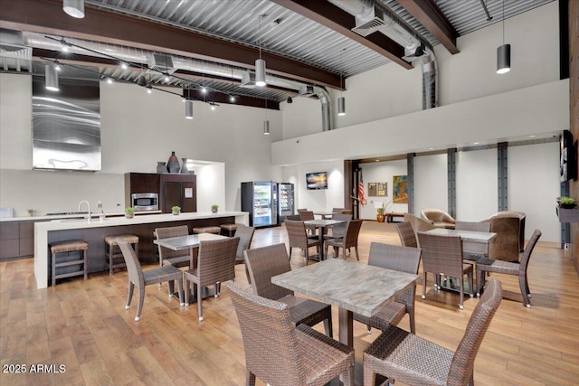 dining room with beam ceiling, light wood-style floors, a towering ceiling, and rail lighting