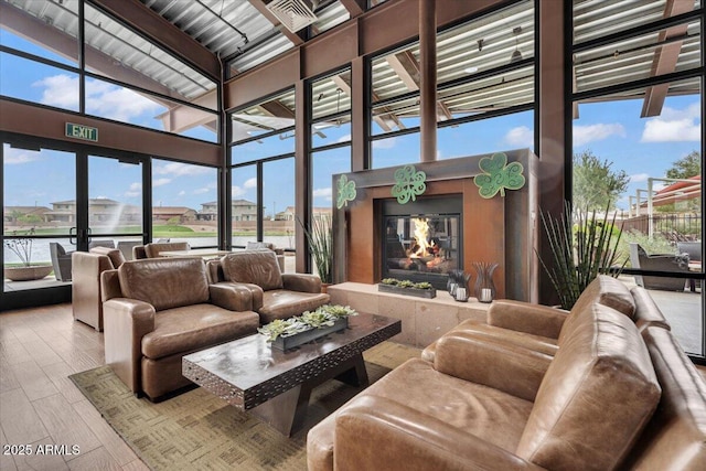 living area featuring a fireplace, a wall of windows, a towering ceiling, and wood finished floors