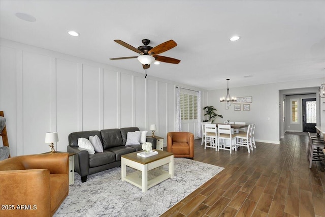 living room with dark wood-style floors, a decorative wall, ceiling fan with notable chandelier, and recessed lighting