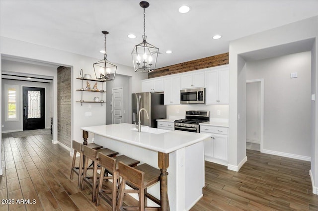 kitchen featuring a kitchen island with sink, dark wood finished floors, stainless steel appliances, white cabinets, and a chandelier