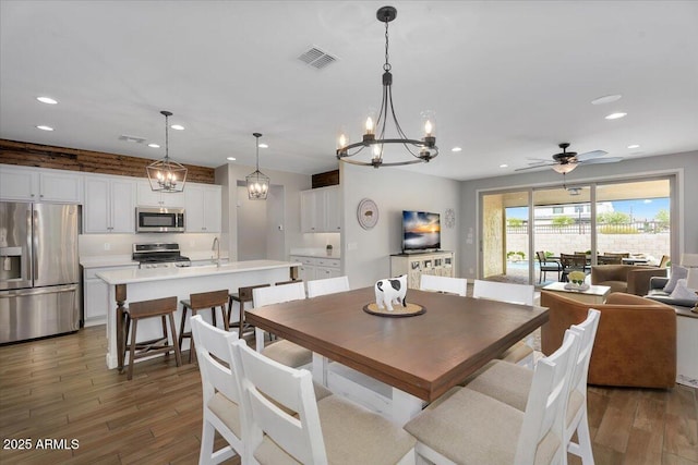 dining space with ceiling fan with notable chandelier, recessed lighting, wood finished floors, and visible vents