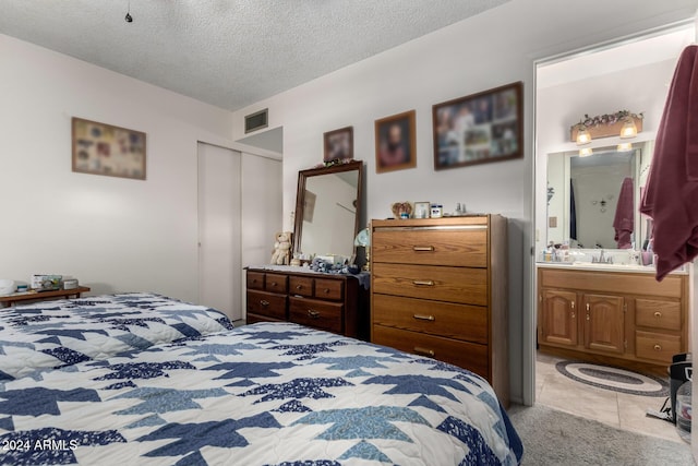 tiled bedroom featuring ensuite bathroom, sink, and a textured ceiling