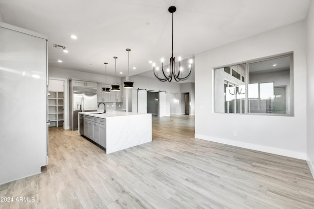 kitchen featuring an island with sink, pendant lighting, a barn door, light hardwood / wood-style flooring, and gray cabinets