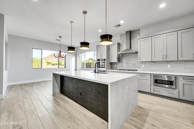 kitchen featuring a kitchen island with sink, wall chimney exhaust hood, hanging light fixtures, and gray cabinets