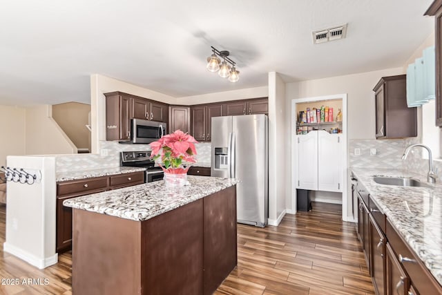 kitchen with sink, stainless steel appliances, light stone counters, a kitchen island, and dark hardwood / wood-style flooring