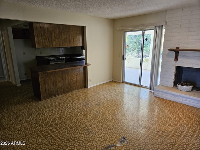 kitchen featuring tile patterned floors, dark countertops, a textured ceiling, a peninsula, and a brick fireplace