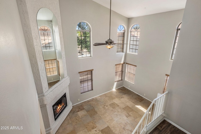 entryway featuring baseboards, a ceiling fan, a glass covered fireplace, stone finish flooring, and arched walkways