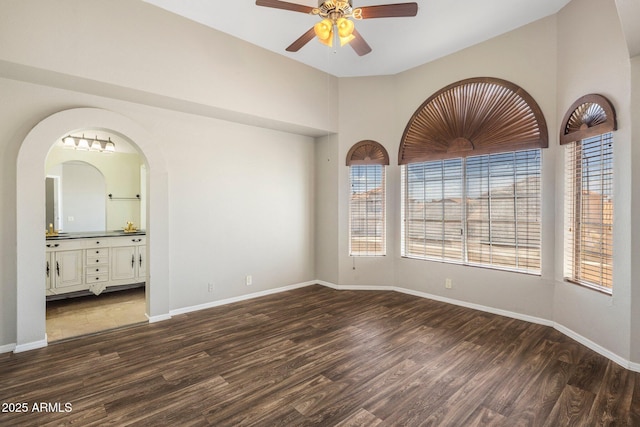 unfurnished room with a ceiling fan, dark wood-style floors, baseboards, arched walkways, and high vaulted ceiling
