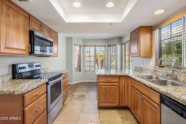 kitchen with appliances with stainless steel finishes, a tray ceiling, a sink, baseboards, and plenty of natural light