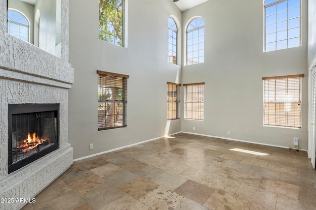 unfurnished living room featuring stone tile flooring, baseboards, a high ceiling, and a lit fireplace