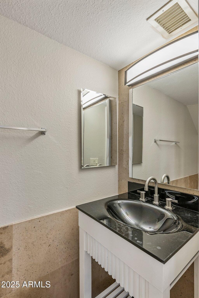bathroom with a textured ceiling, vanity, and a textured wall