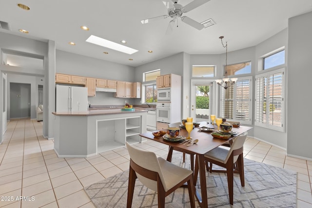 dining space with ceiling fan with notable chandelier, a skylight, sink, and light tile patterned floors