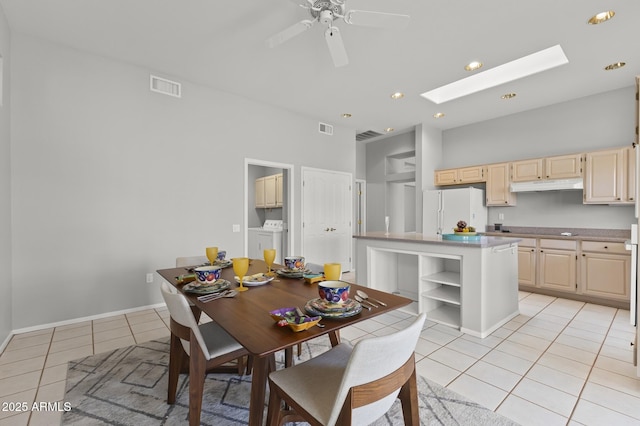 tiled dining room featuring a skylight, independent washer and dryer, ceiling fan, and a high ceiling