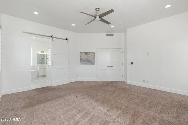 carpeted spare room featuring a barn door and ceiling fan